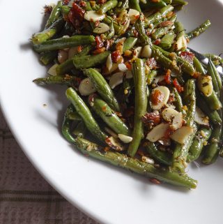 Cooked green beans, slivered almonds, and bacon served on plate.