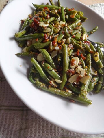 Cooked green beans, slivered almonds, and bacon served on plate.