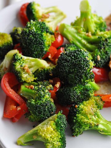 Cooked broccoli with red pepper slices on plate ready to serve.