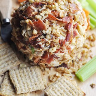 Cheese ball covered with bacon and walnuts served on wooden tray with celery, carrots, and crackers.