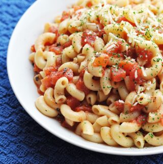Cooked macaroni with diced tomatoes in white bowl ready to eat.