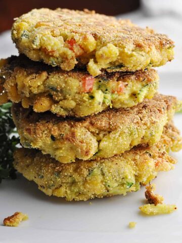 Four corn zucchini fritters with red peppers and cheese stacked on plate.