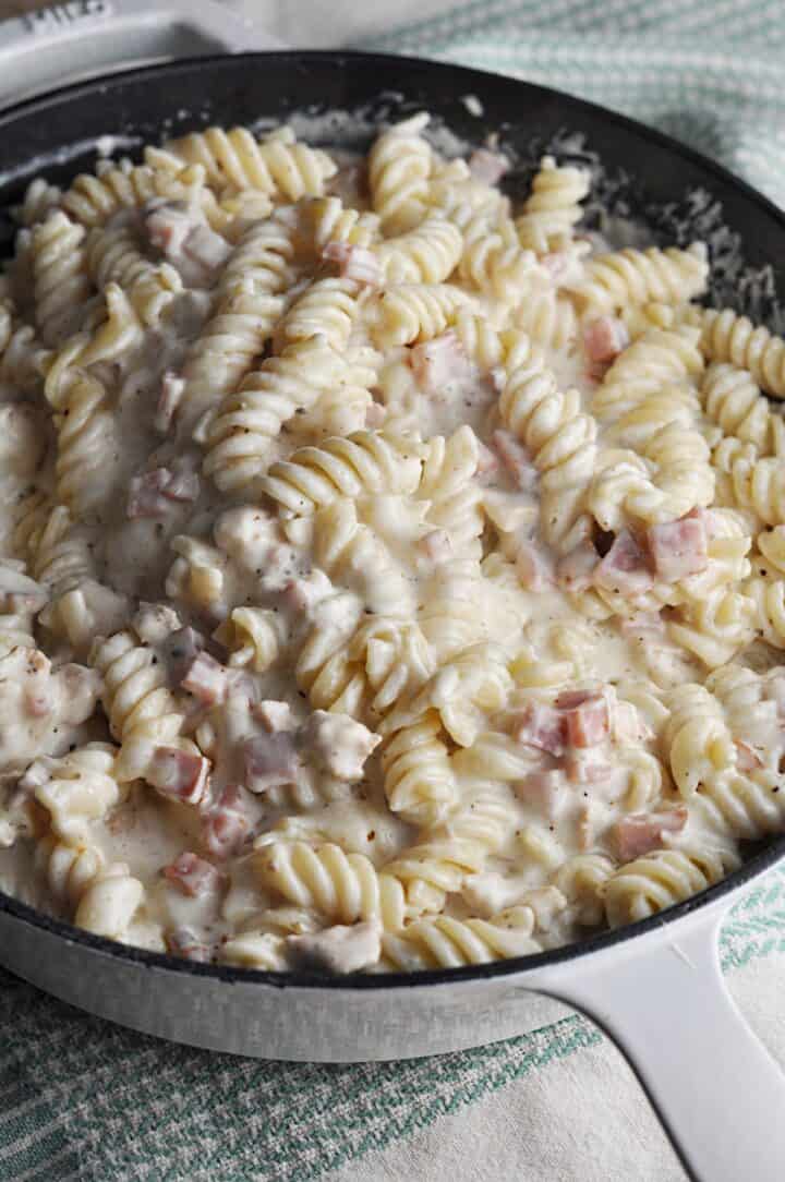 Cast iron skillet with pasta dinner including ham and chicken and creamy sauce