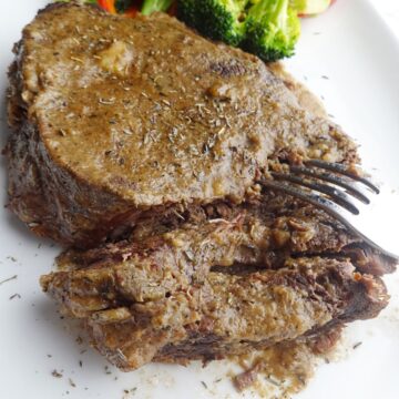 Cooked beef roast on platter with fork.