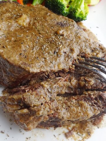 Cooked beef roast on platter with fork.