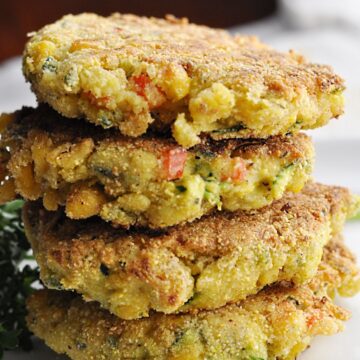 Four corn zucchini fritters with red peppers stacked on plate.