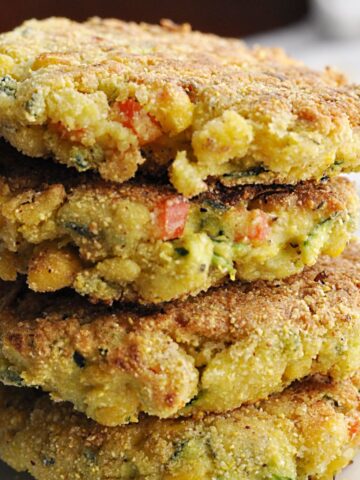 Four corn zucchini fritters with red peppers stacked on plate.