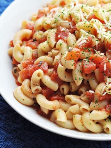 Macaroni pasta with diced tomatoes and parmesan cheese in white bowl ready to eat.