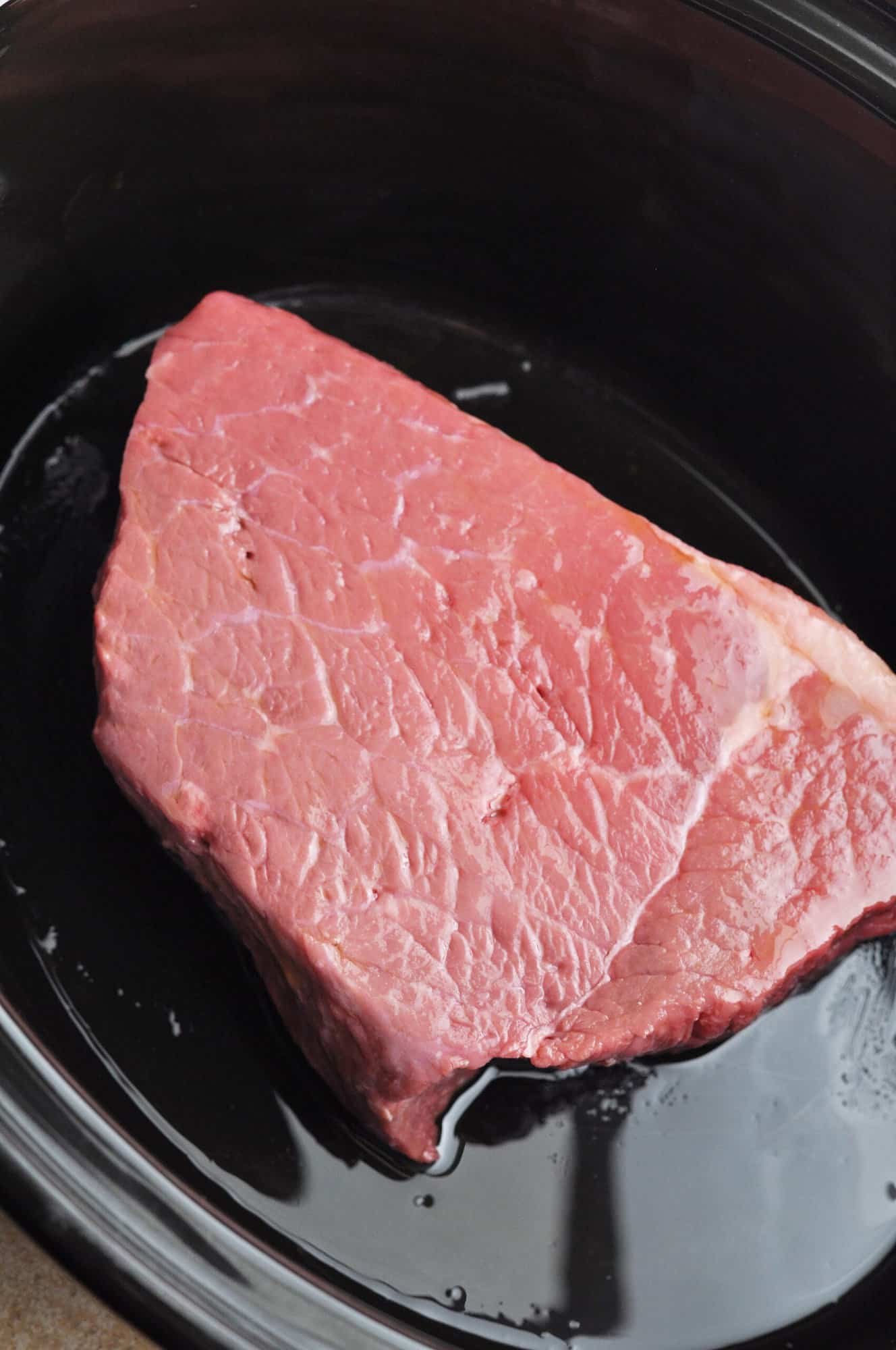 Raw beef roast in slow cooker ready to cook.