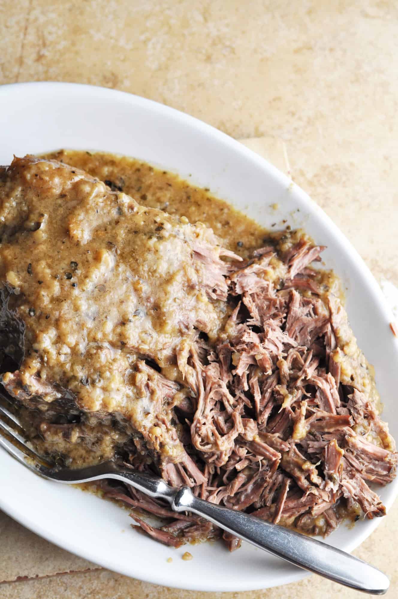 Fork-tender beef roast on plate with gravy.