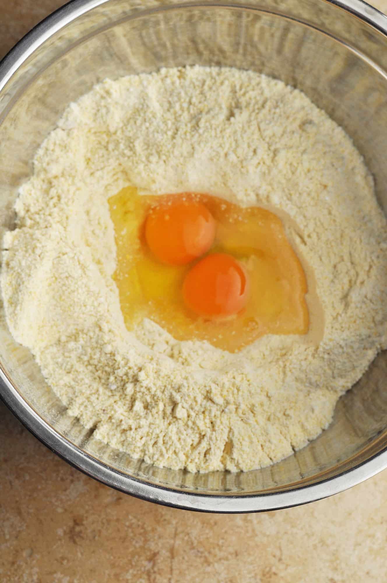 Raw eggs in a bowl in the center of cornmeal mixture.