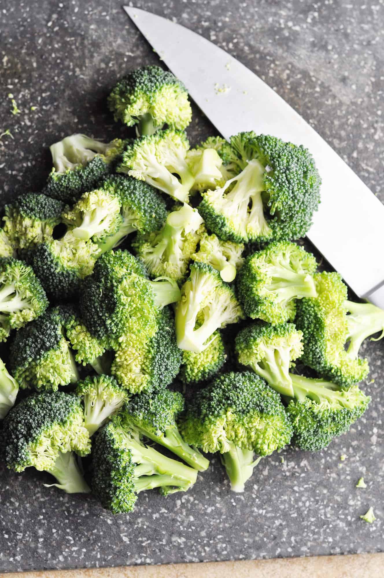 Chopped raw broccoli on cutting board with knife.