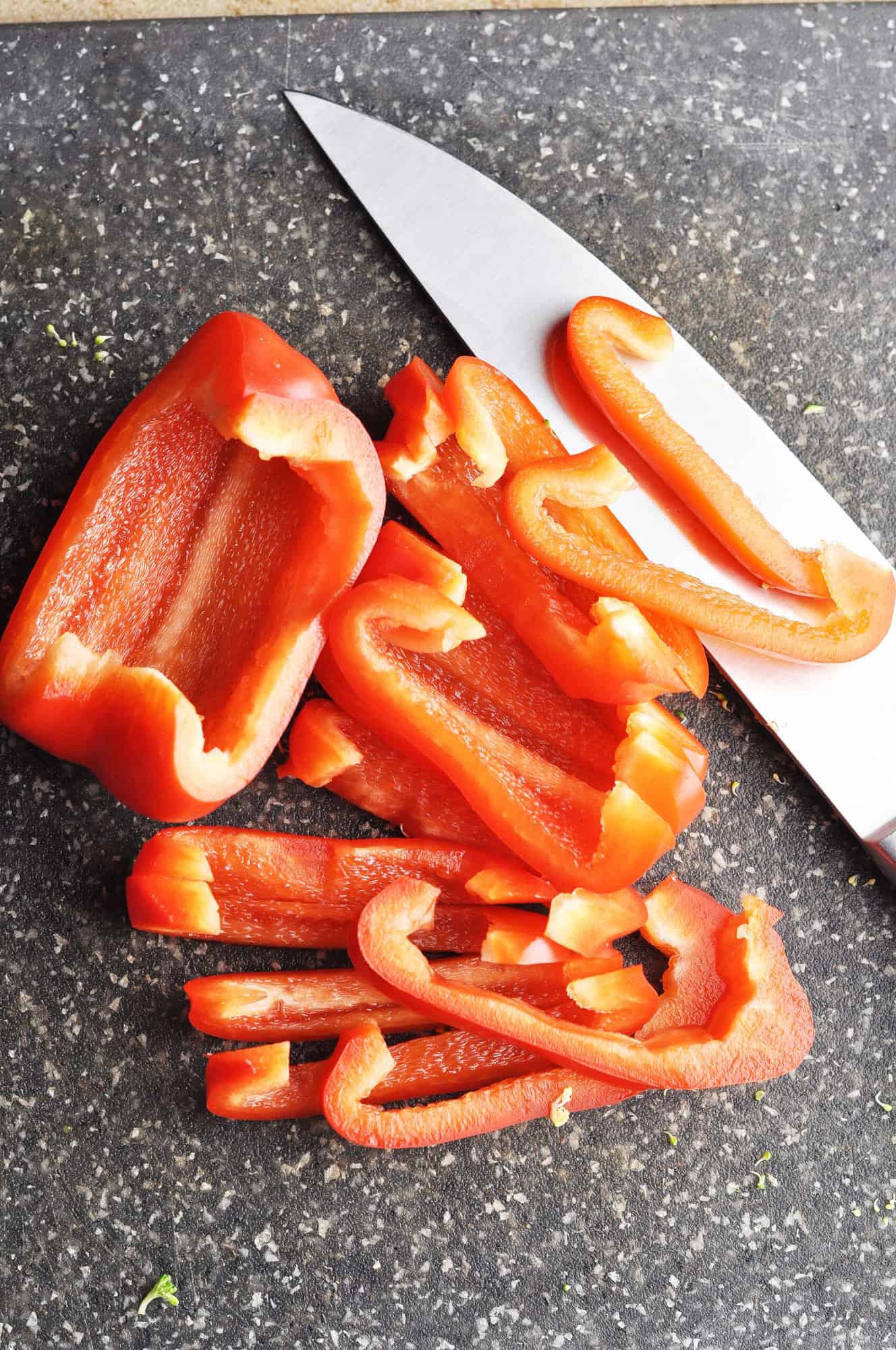Sliced red bell pepper on cutting board with knife.