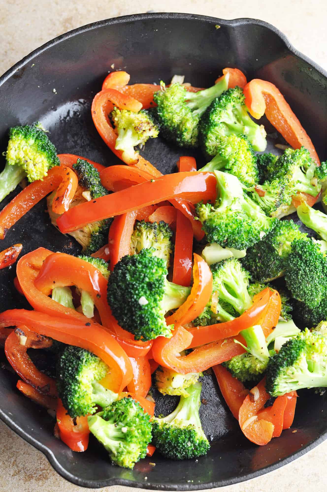 Cooked broccoli with red peppers and garlic in cast iron skillet.