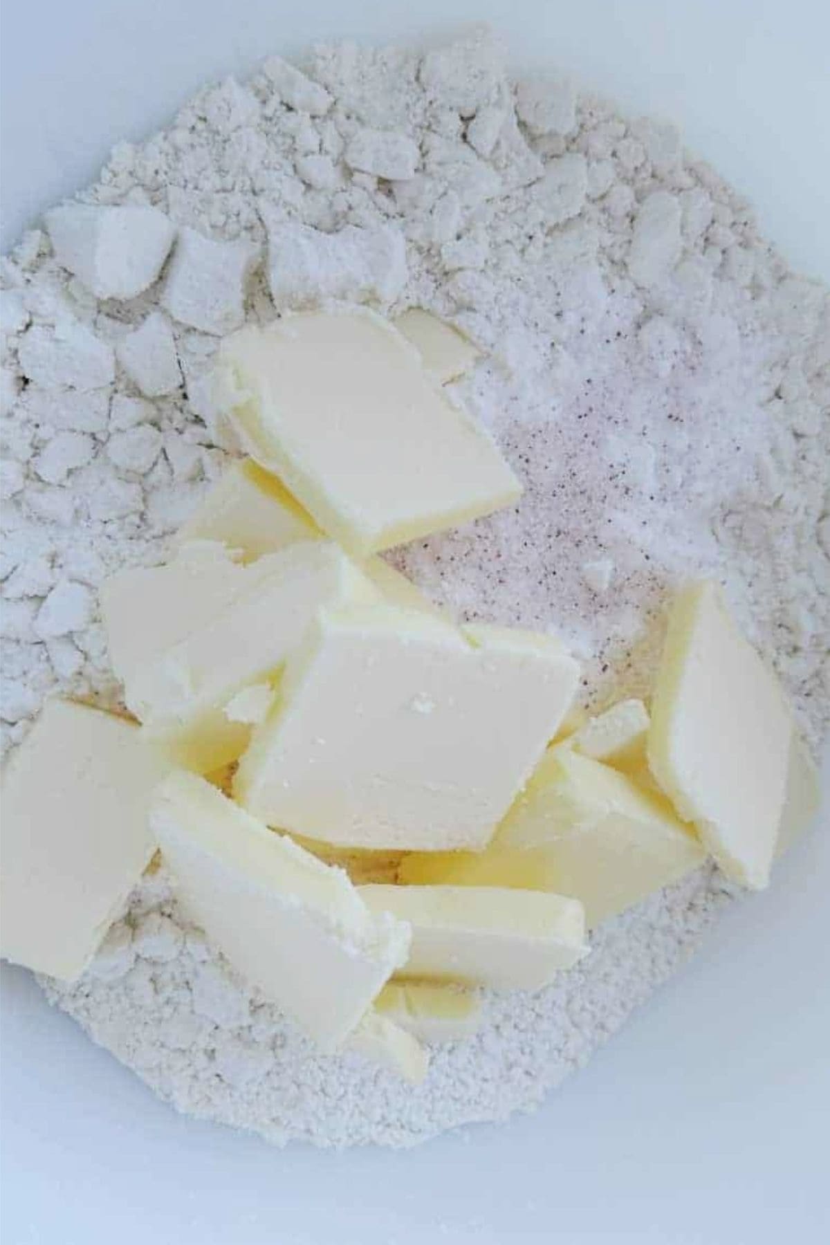 Flour, baking powder, and salt in large bowl with butter pieces on top.