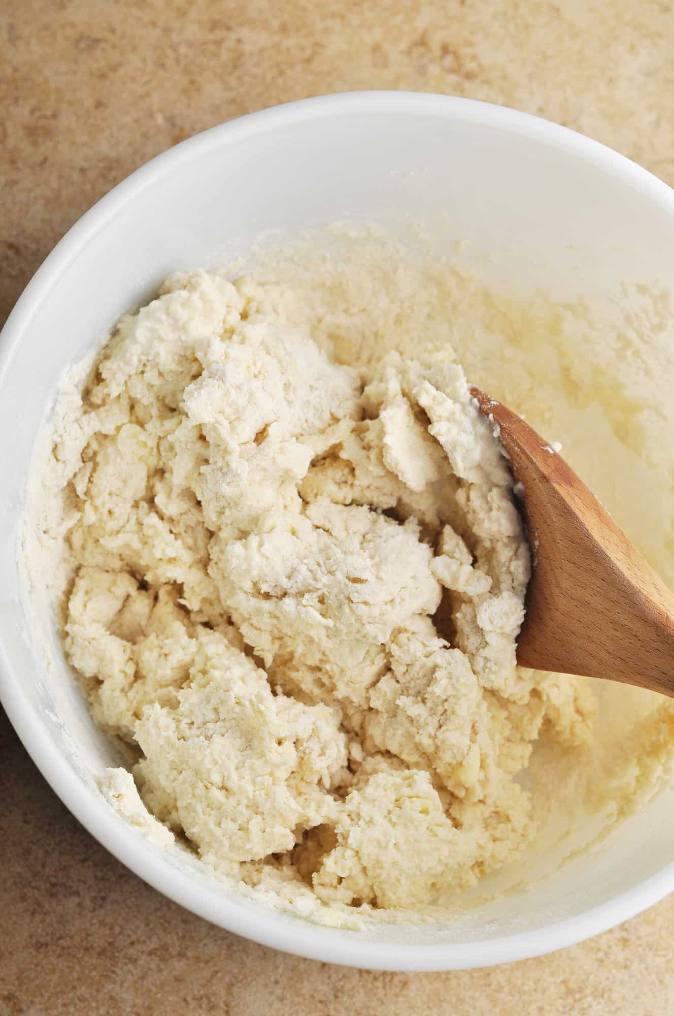 Biscuit dough in large bowl with wooden spoon.