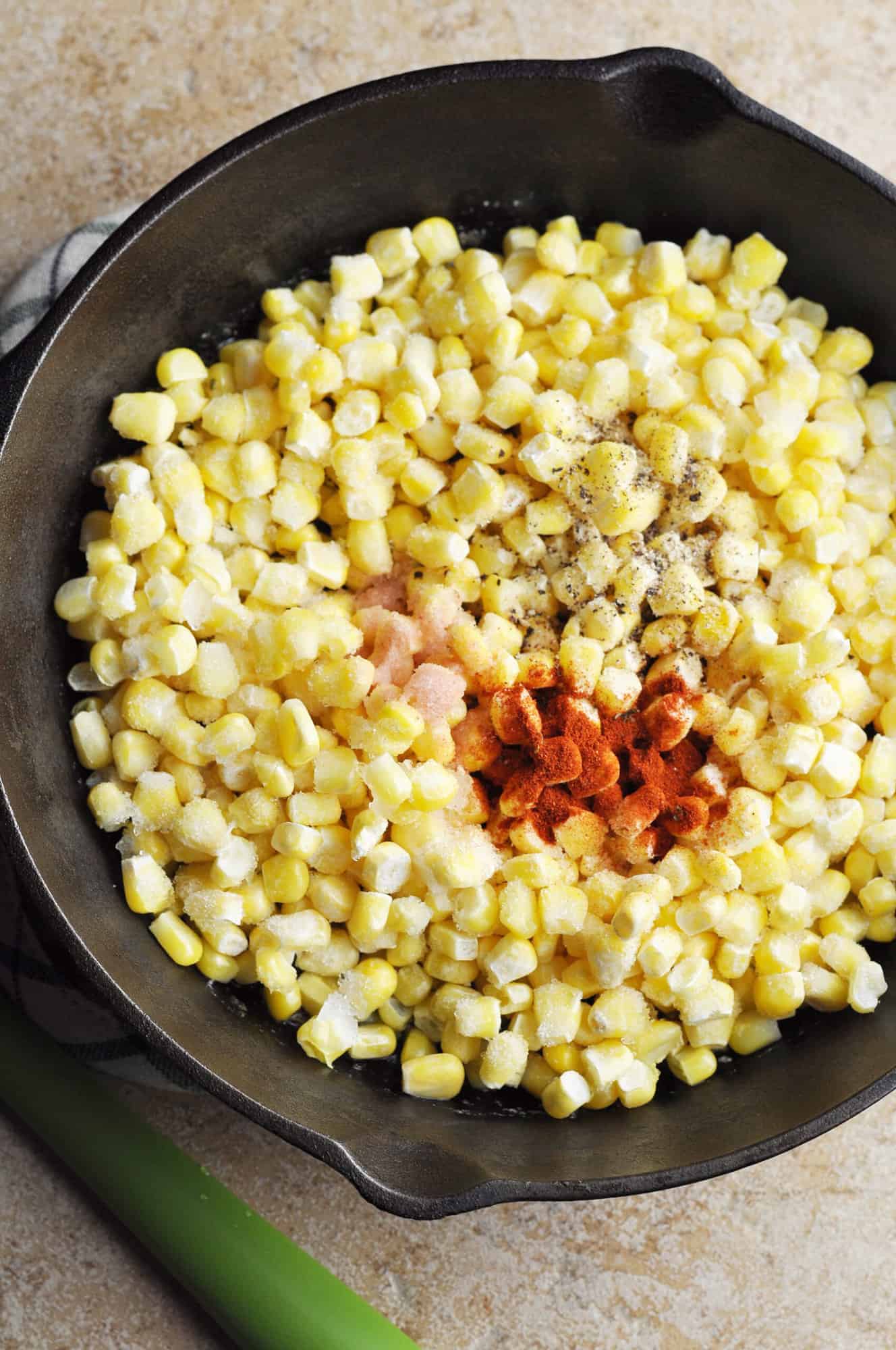 Frozen corn in cast iron skillet with salt, black pepper, and paprika.
