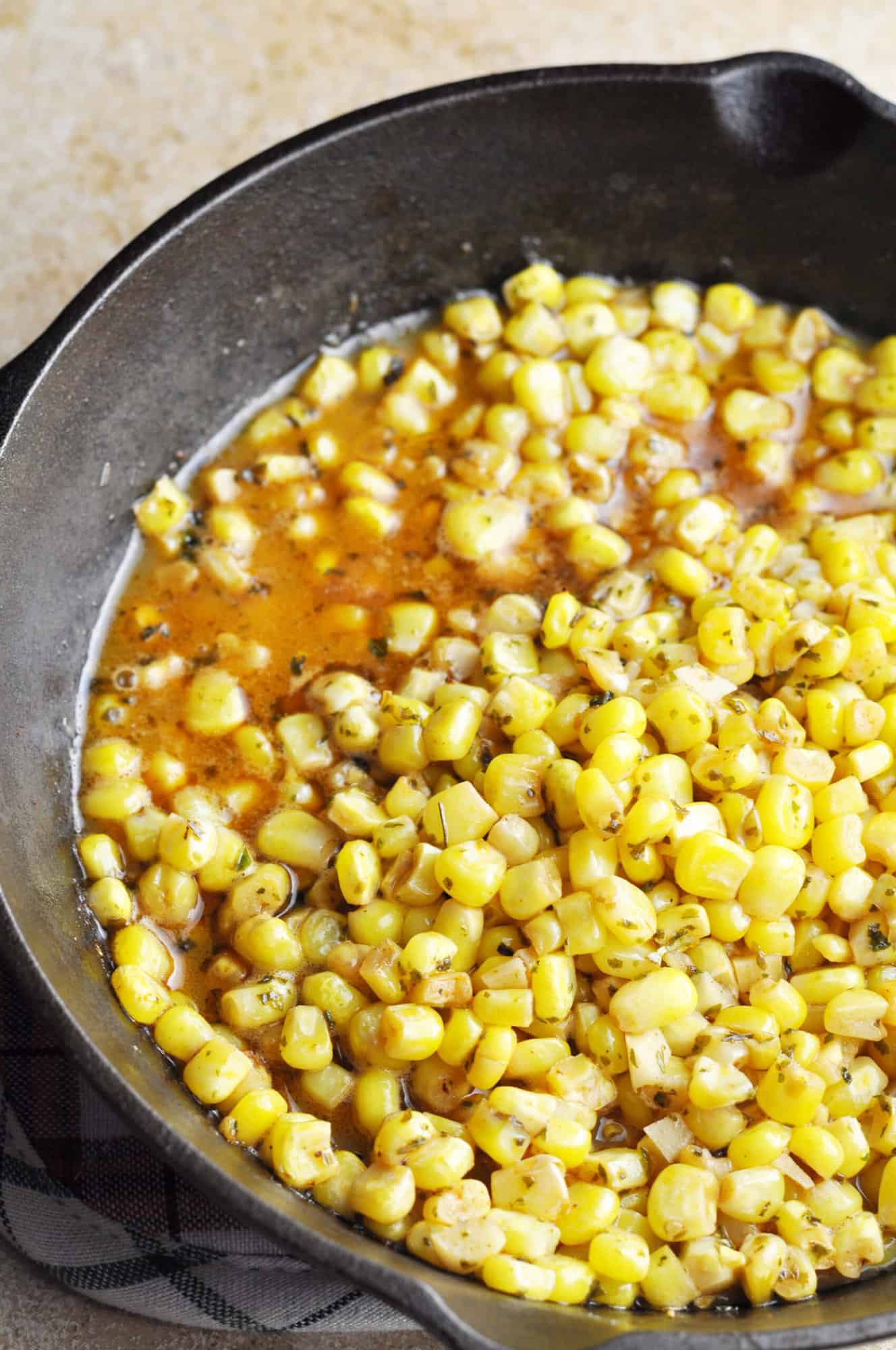 Corn with chicken broth, herbs, and paprika in cast iron pan.