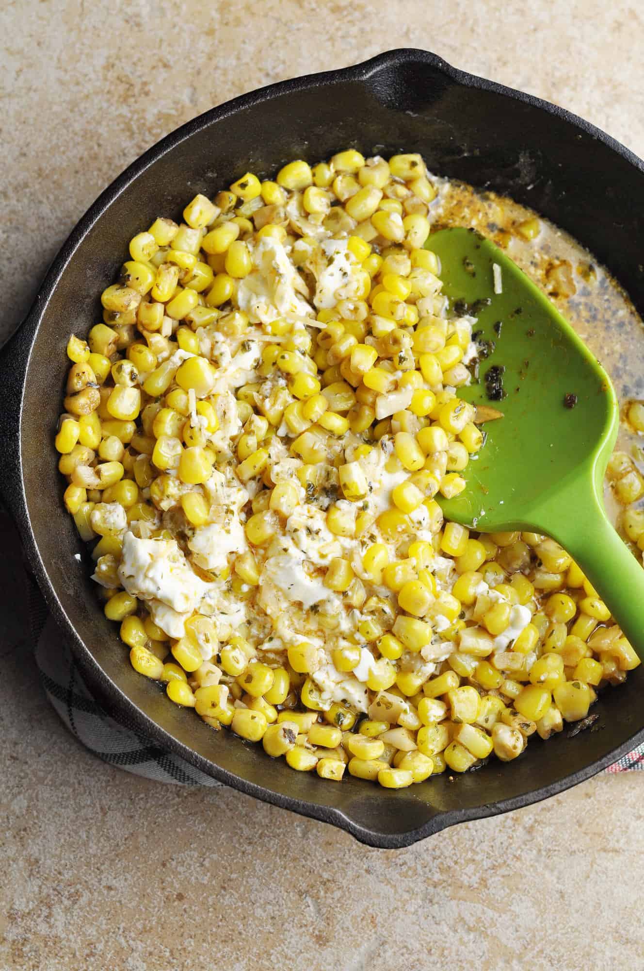 Corn, chicken broth, cream cheese, and parmesan cheese in cast iron pan with spatula.
