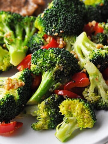 Cooked broccoli with red bell pepper slices and garlic on plate.