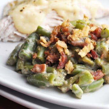 Green bean casserole topped with fried onions and bacon on plate with turkey covered in gravy.