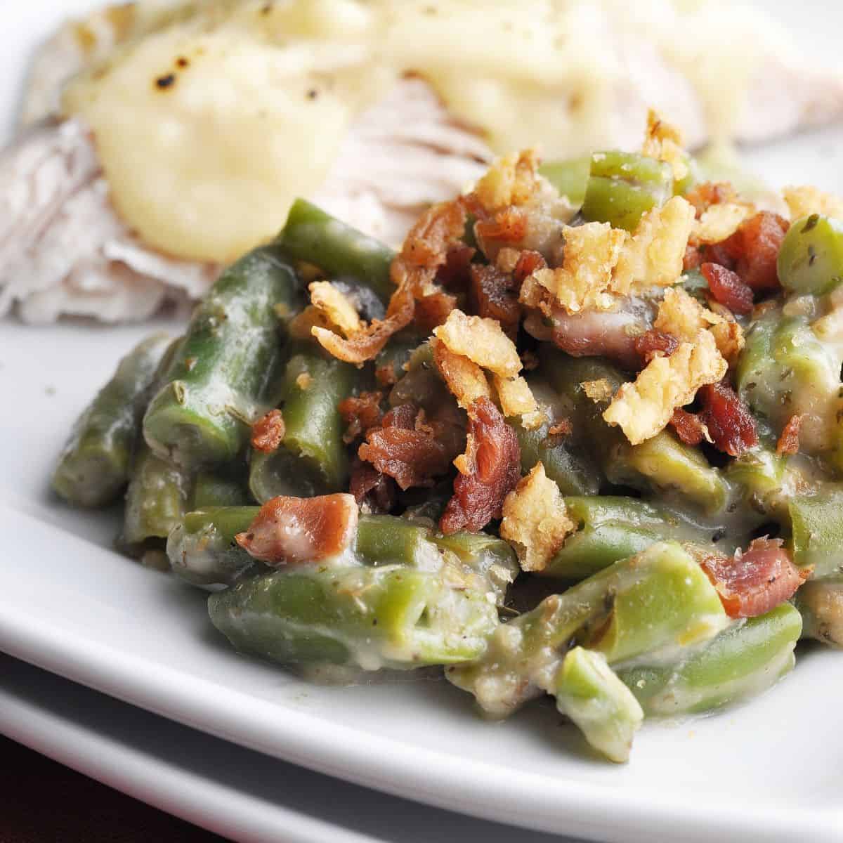 Green bean casserole topped with fried onions and bacon on plate with turkey covered in gravy.