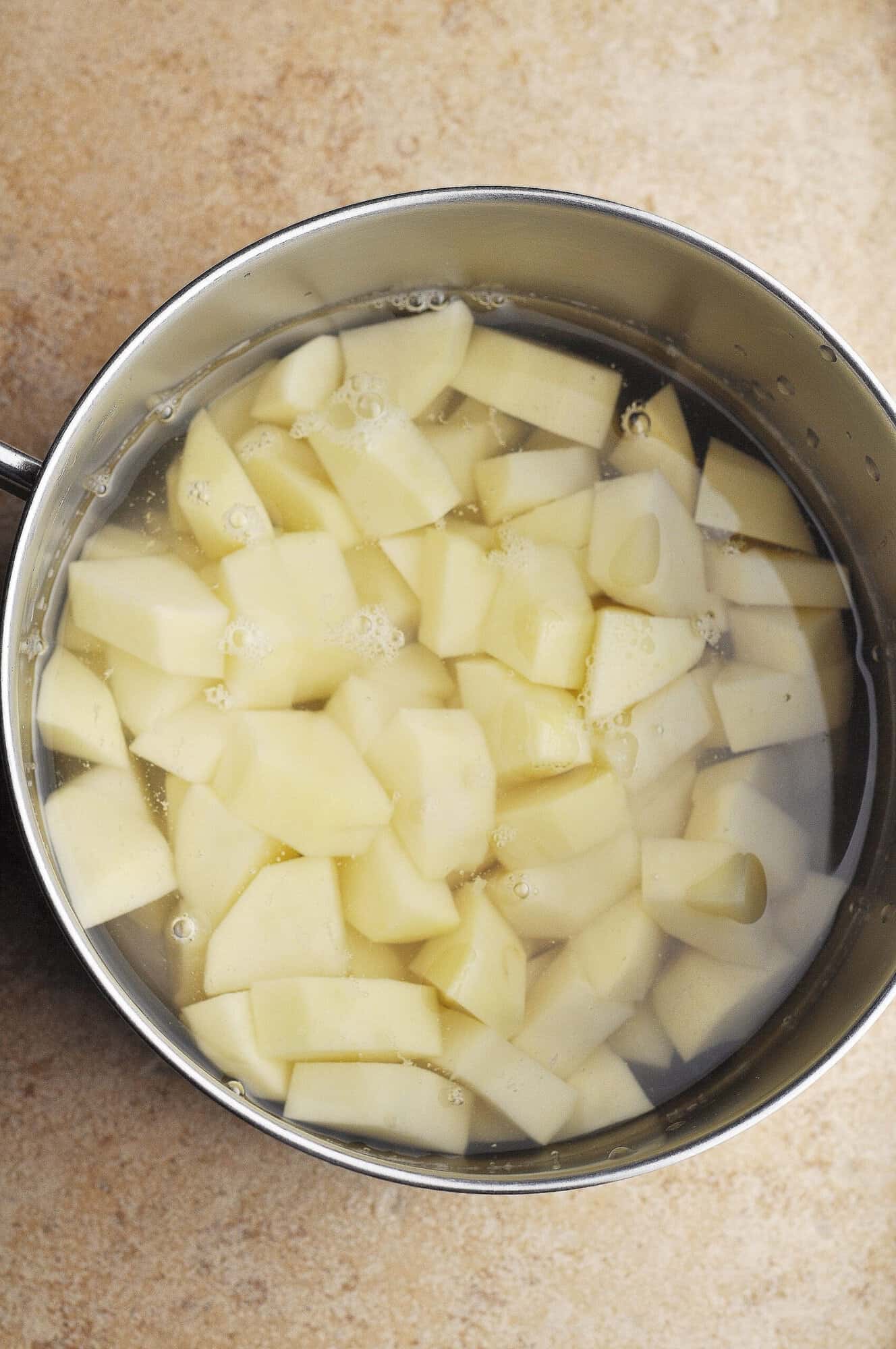 Raw potato chunks in pot covered with water.