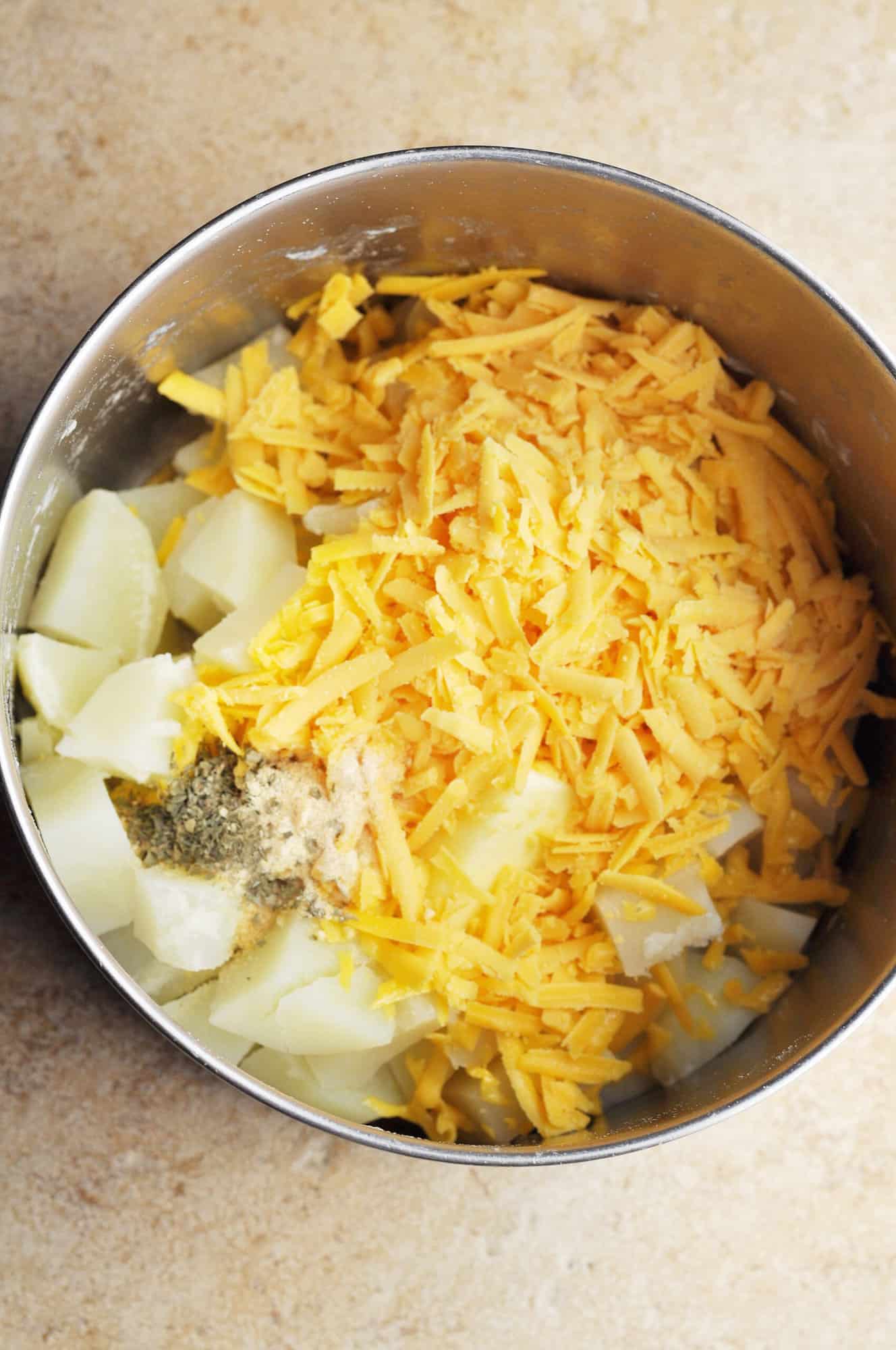 Cooked potatoes with shredded cheese, garlic powder, and dry parsley in pot.