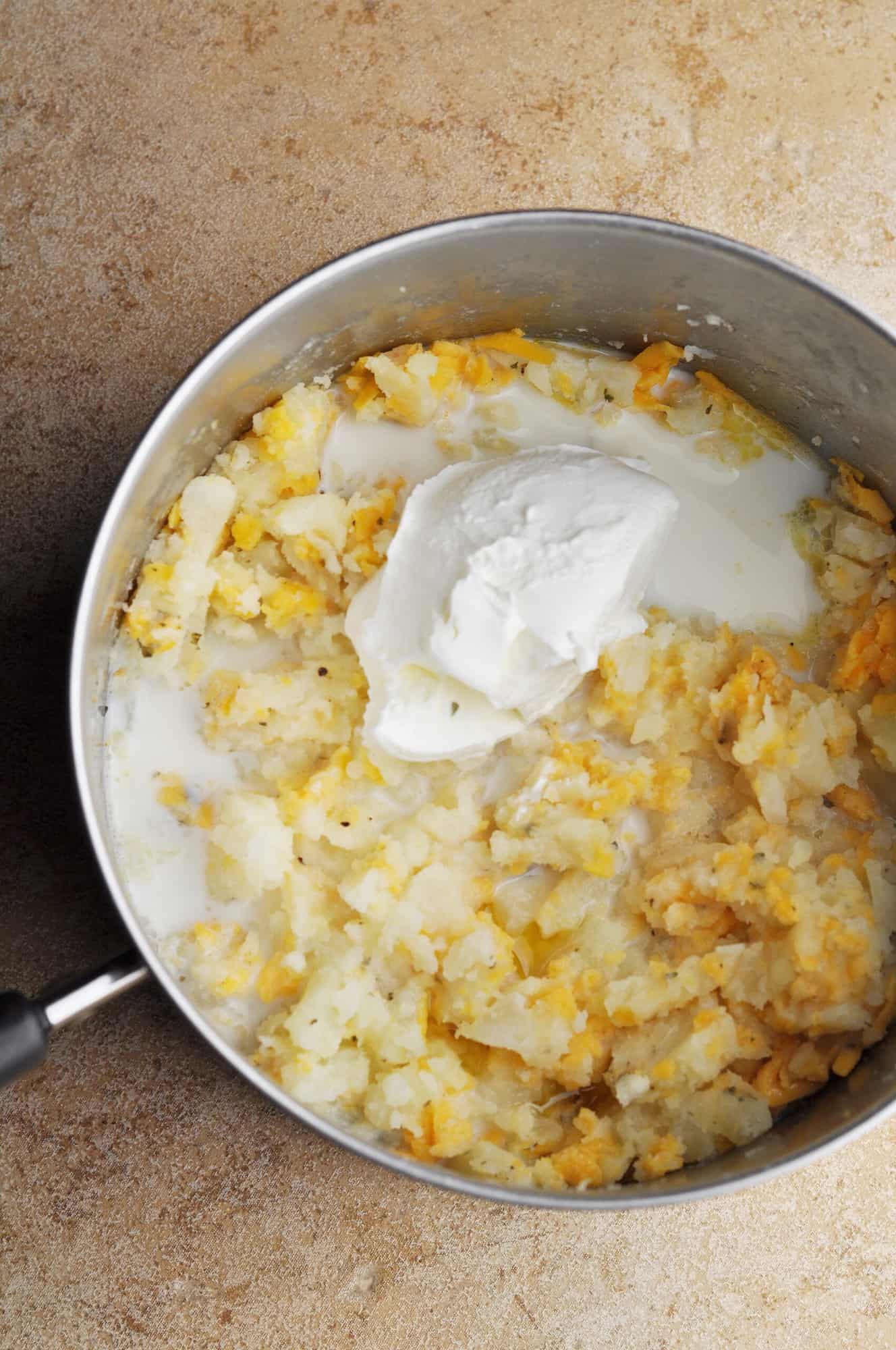 Cooked potatoes, cheese, sour cream, and milk in pot.