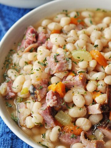 Navy bean and ham soup with celery and carrots served in bowl.