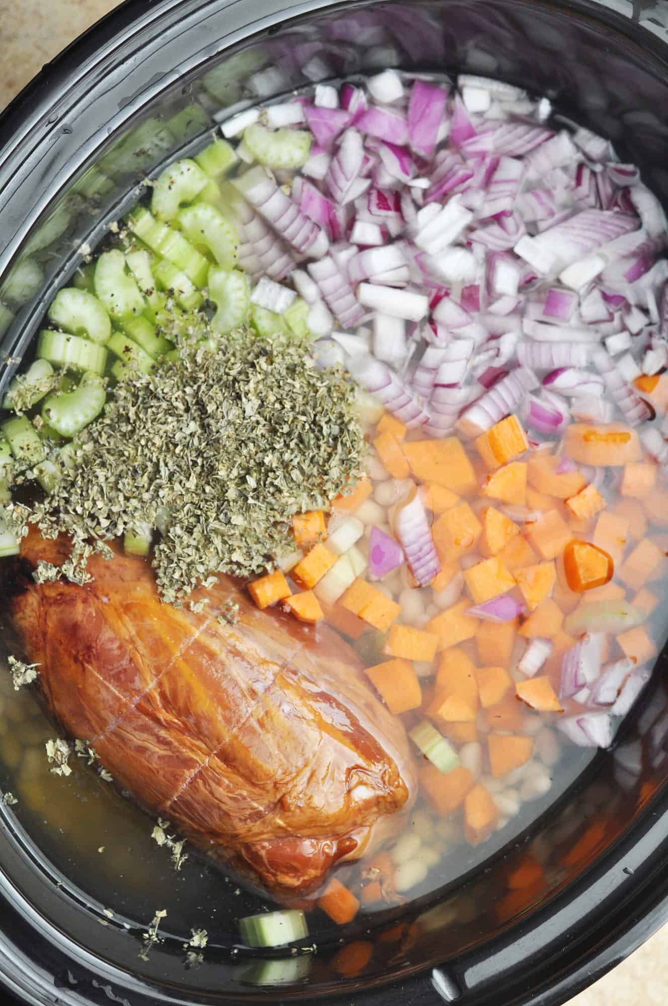 Dry beans, ham hock, chopped carrot, chopped celery, chopped onion, dry herbs, and water in slow cooker ready to cook.