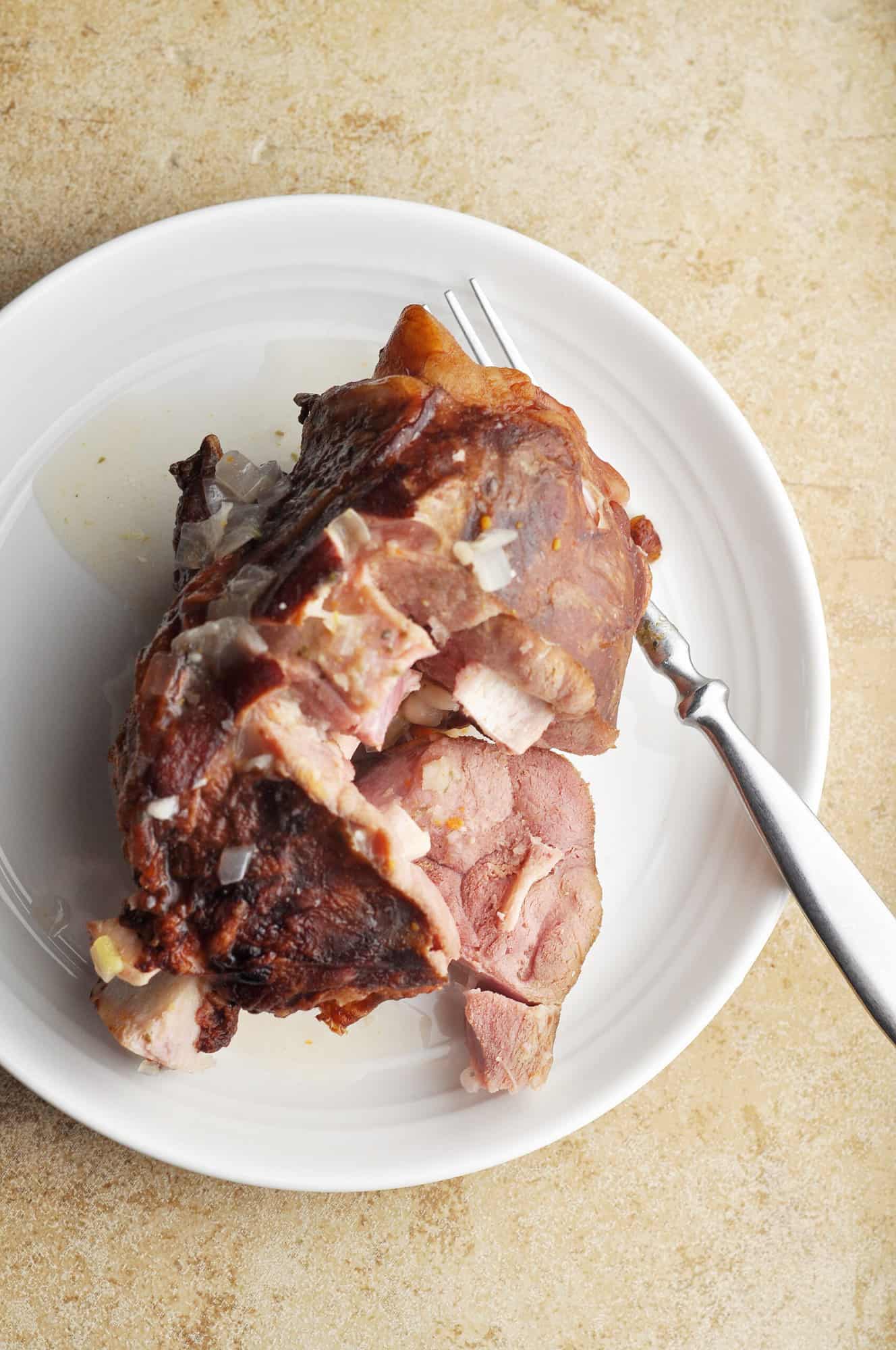 Ham hock on plate with ham being pulled off with fork.