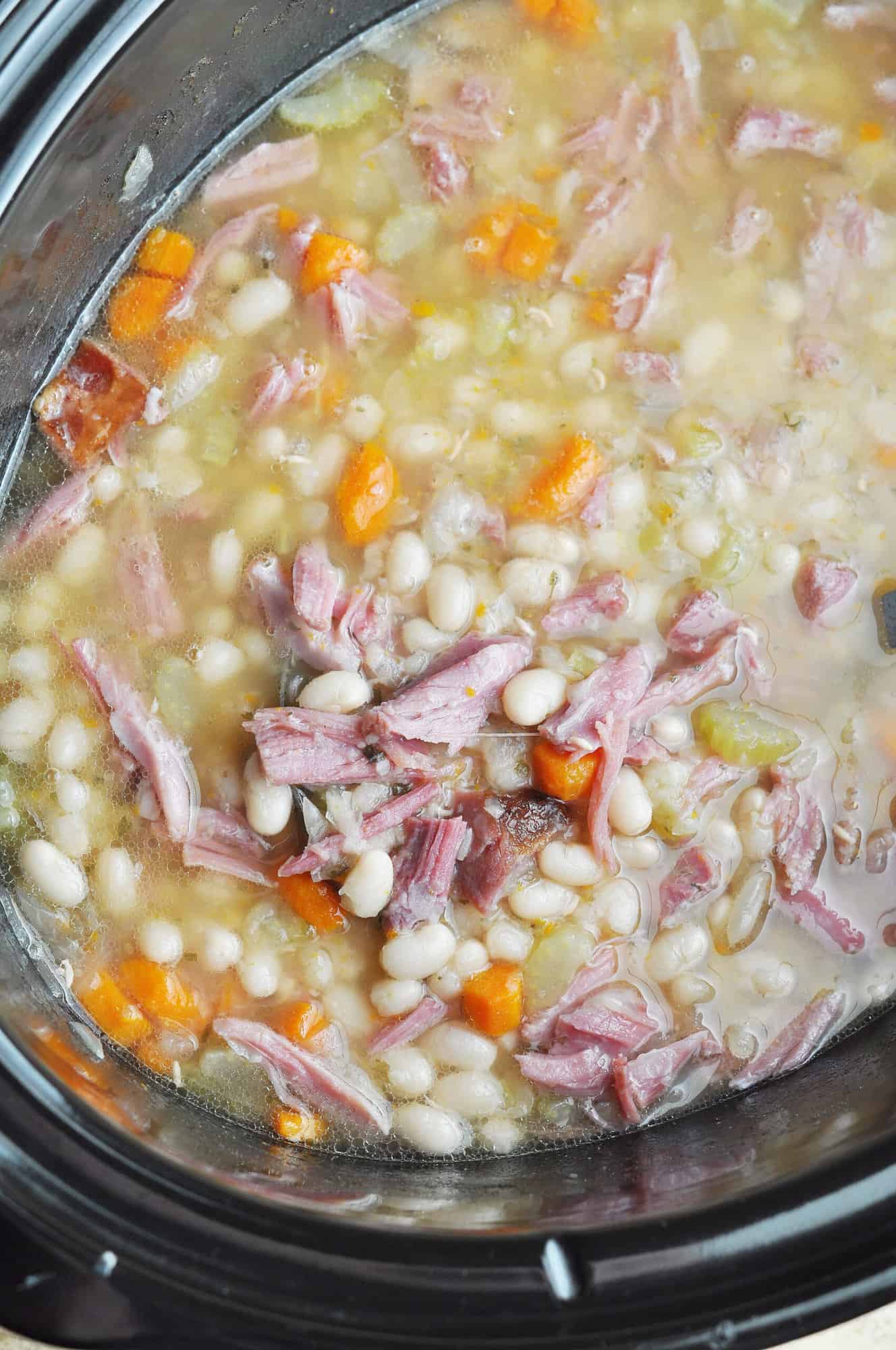 Navy bean soup with carrots, celery, and ham in slow cooker.